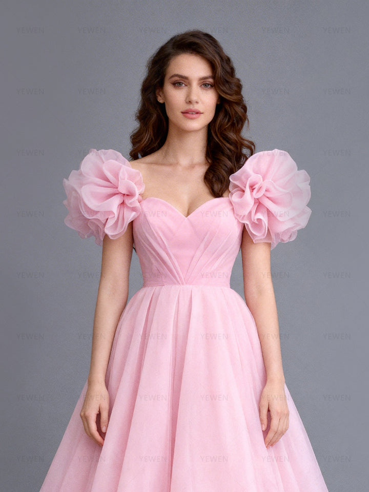 Close-up front view of a model wearing a blush tulle evening dress highlighting the sweetheart neckline and layered puff sleeves.