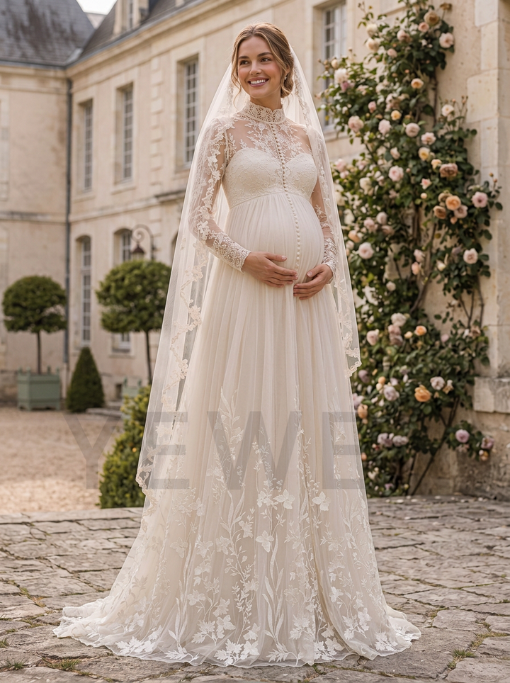 A pregnant woman wearing a long-sleeved ivory lace wedding gown with a matching lace veil, standing outdoors in front of a stone building with rose vines.