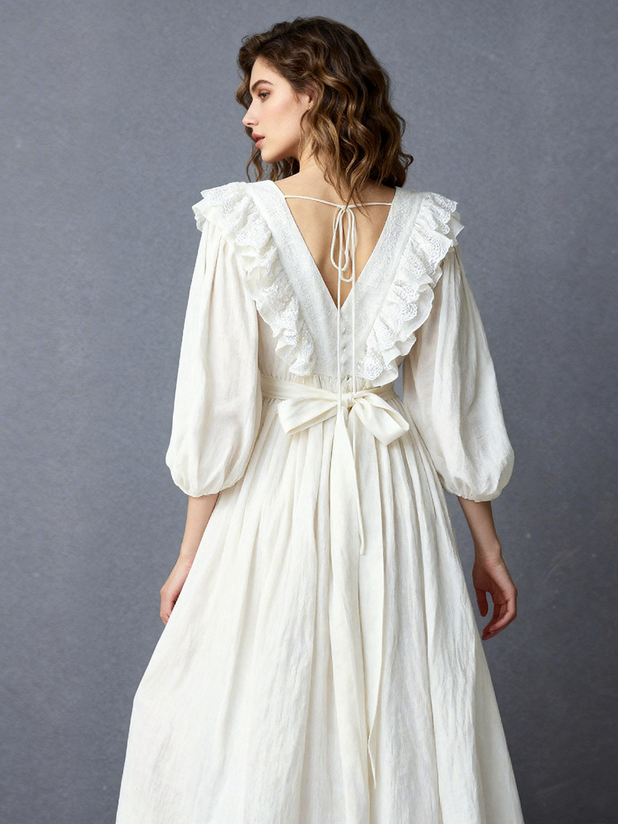 Back view of a model wearing an ivory boho sheer maxi dress with a deep V-back tie detail and ruffle-trimmed balloon sleeves.