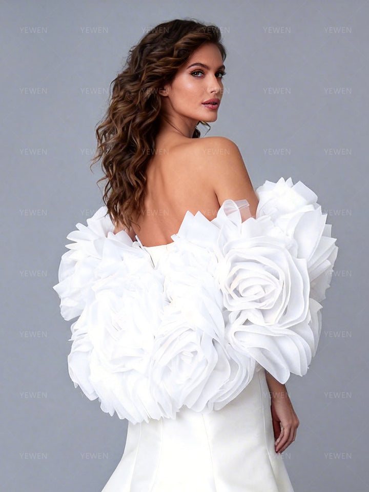 Close-up back view of a model wearing an ivory off-shoulder satin bridal gown highlighting the 3D floral cape and open-back design.