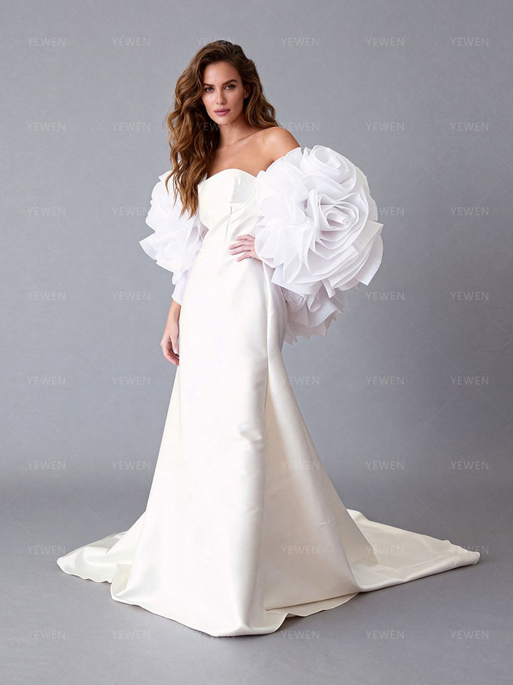 Side view of a model wearing an ivory off-shoulder satin bridal gown with a 3D floral cape and sweeping train.