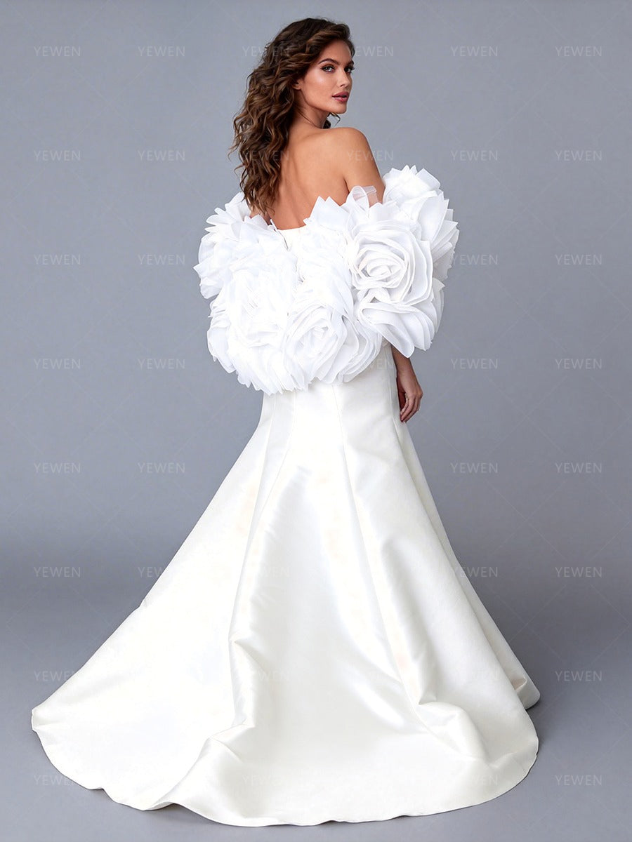 Back view of a model wearing an ivory off-shoulder satin bridal gown with a 3D floral cape and sweeping train.
