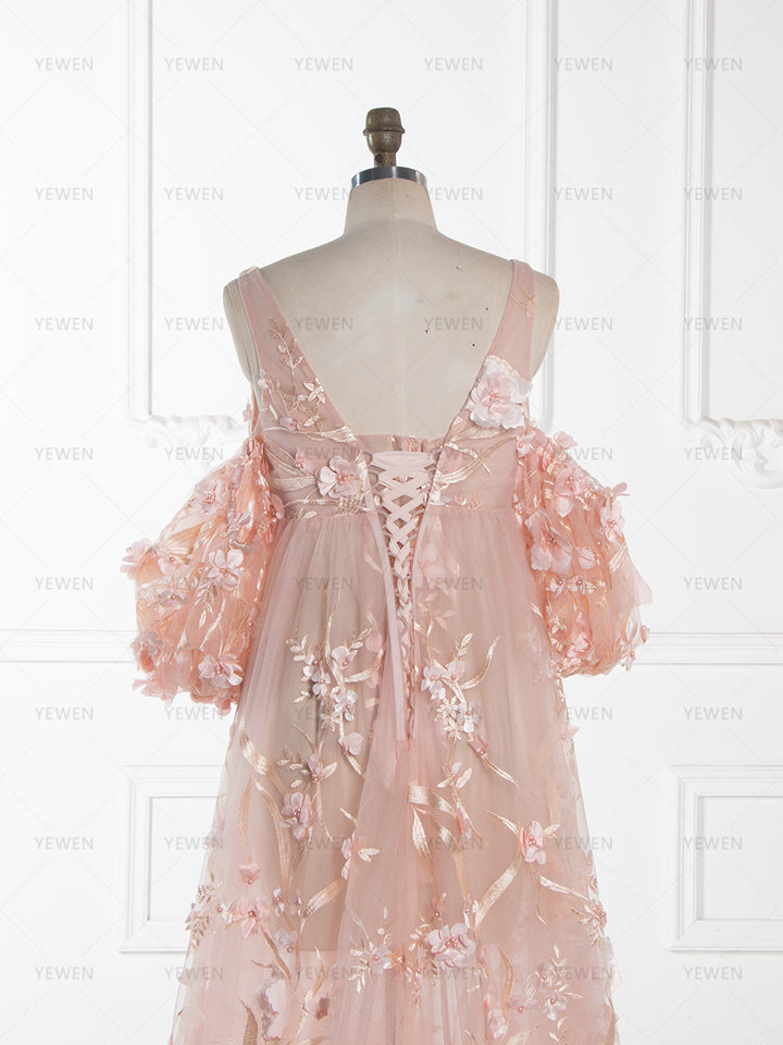Close-up back detail of a light pink lace maternity dress, featuring an open-back design with a lace-up closure and 3D floral appliques scattered on the sheer fabric and sleeves.