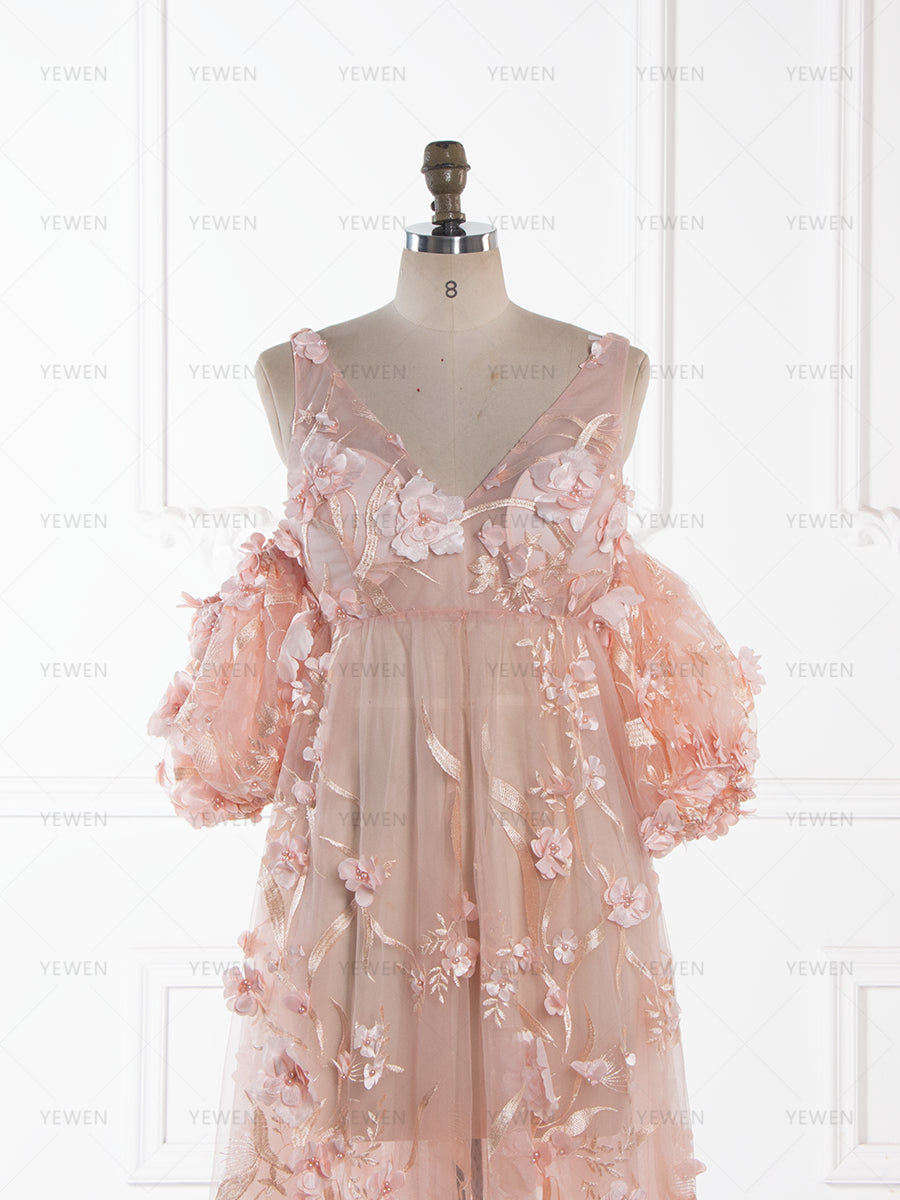 Close-up front detail of a light pink sheer lace maternity dress, highlighting the deep V-neckline, the clustered 3D floral appliques on the bodice, and the voluminous off-shoulder puffed sleeves.