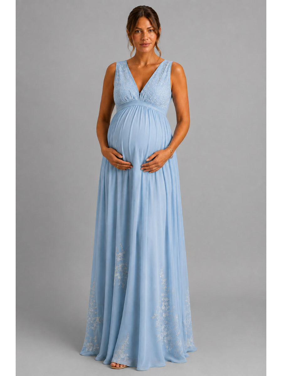 A pregnant woman modeling a sleeveless light blue maternity maxi dress with a lace V-neck bodice and flowing chiffon skirt, standing against a solid gray studio background.