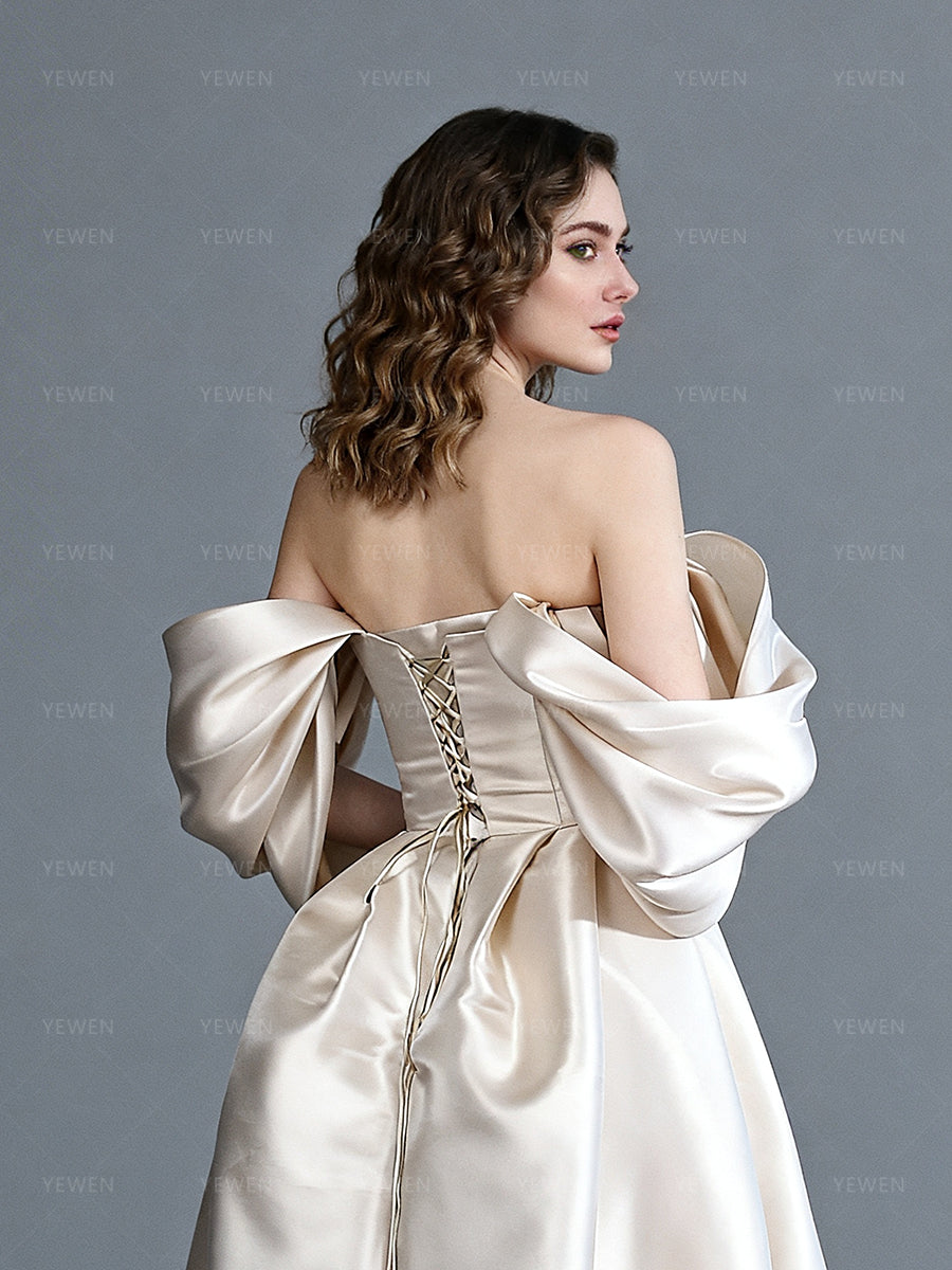 Close-up back view of a model wearing an off-shoulder satin bespoke occasion gown highlighting the lace-up corset back and draped sleeves.