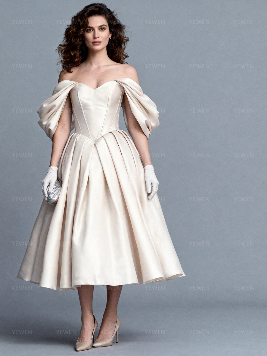 Full front view of a model wearing an off-shoulder satin bespoke occasion gown with a corset bodice and a pleated skirt.