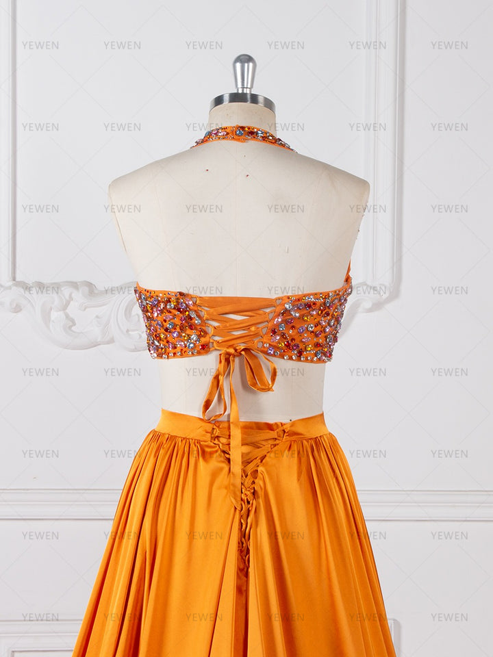 Close-up back view of an orange beaded two-piece evening gown highlighting the halter neck tie and layered skirt details on a mannequin.