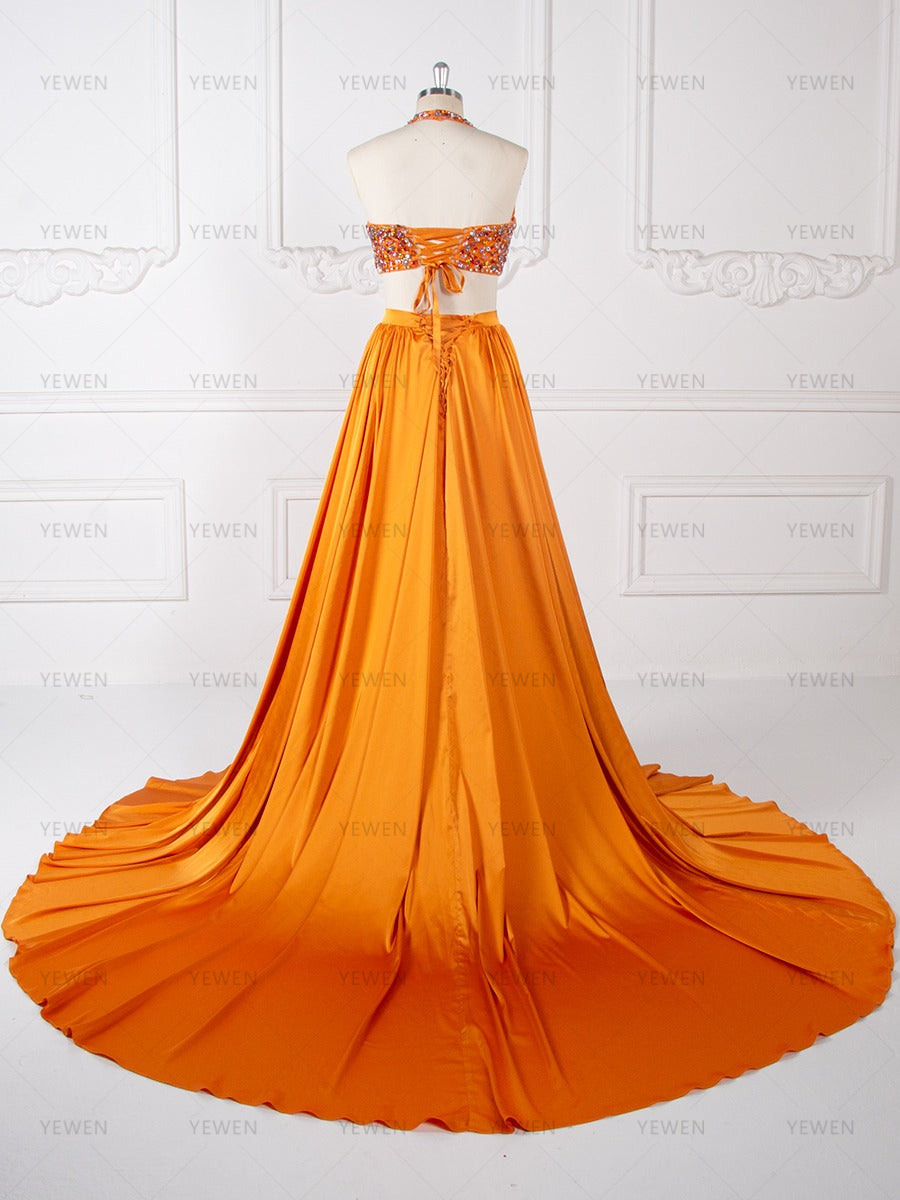 Back view of an orange beaded two-piece evening gown with a flowing pleated maxi skirt displayed on a mannequin.