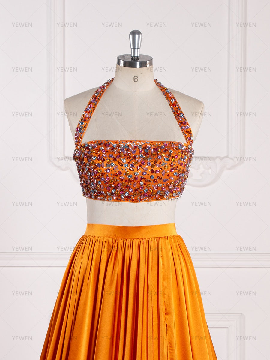 Close-up front view of an orange beaded two-piece evening gown highlighting the halter neckline and beaded crop top on a mannequin.