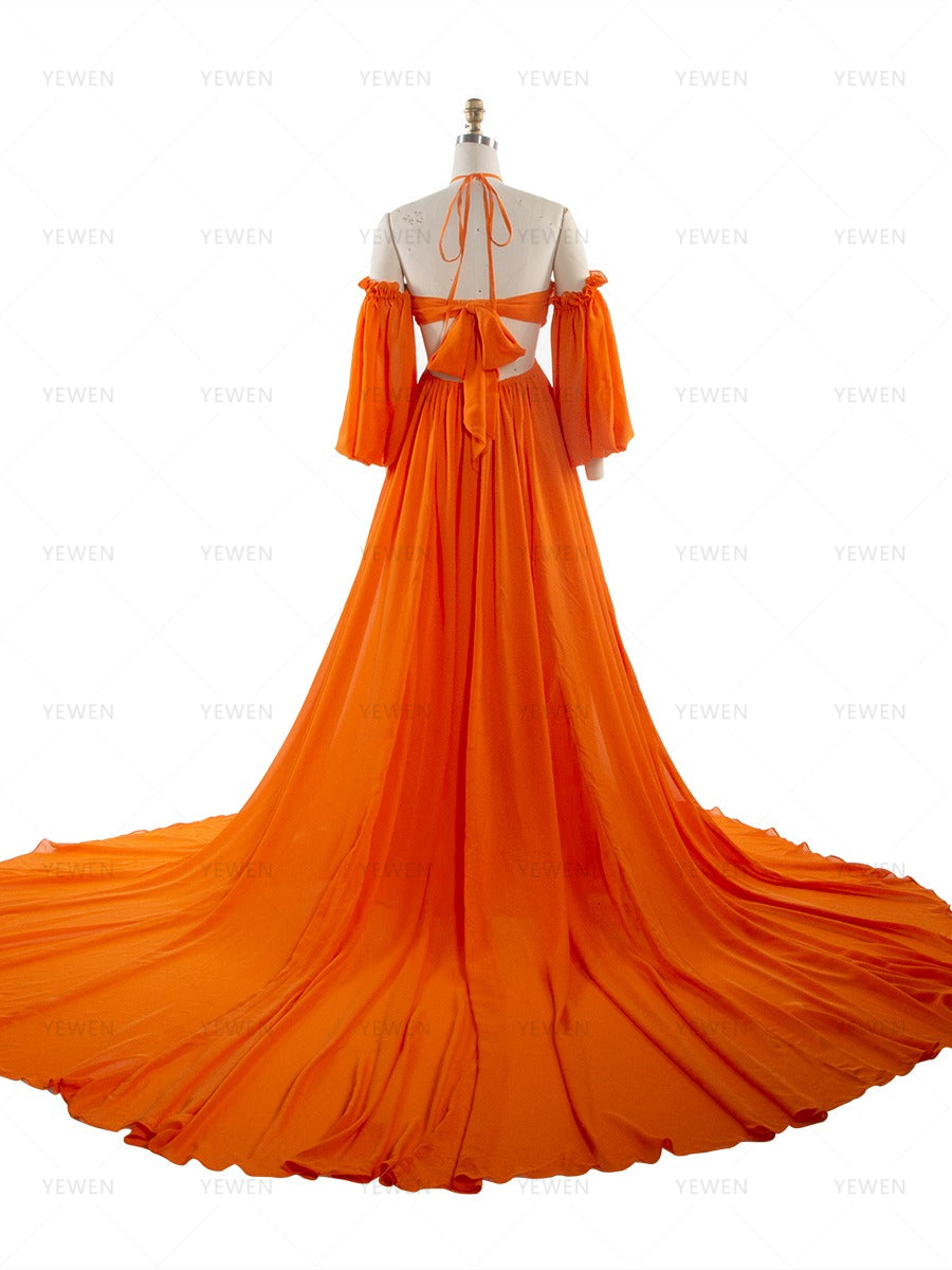 Back full-length view of an orange chiffon boho photoshoot dress with a halter neckline detachable puff sleeves a twisted waist and a side slit displayed on a mannequin.