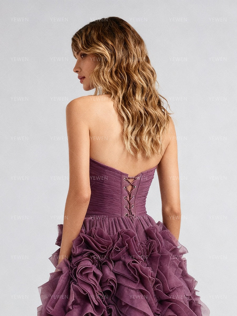 Close-up back view of a model wearing a plum strapless prom dress highlighting the lace-up corset back and ruffled details.