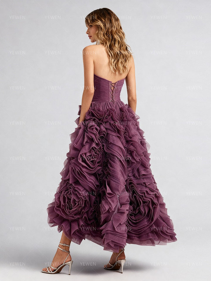 Back view of a model wearing a plum 3D floral strapless prom dress with a lace-up corset back and ruffled midi skirt.