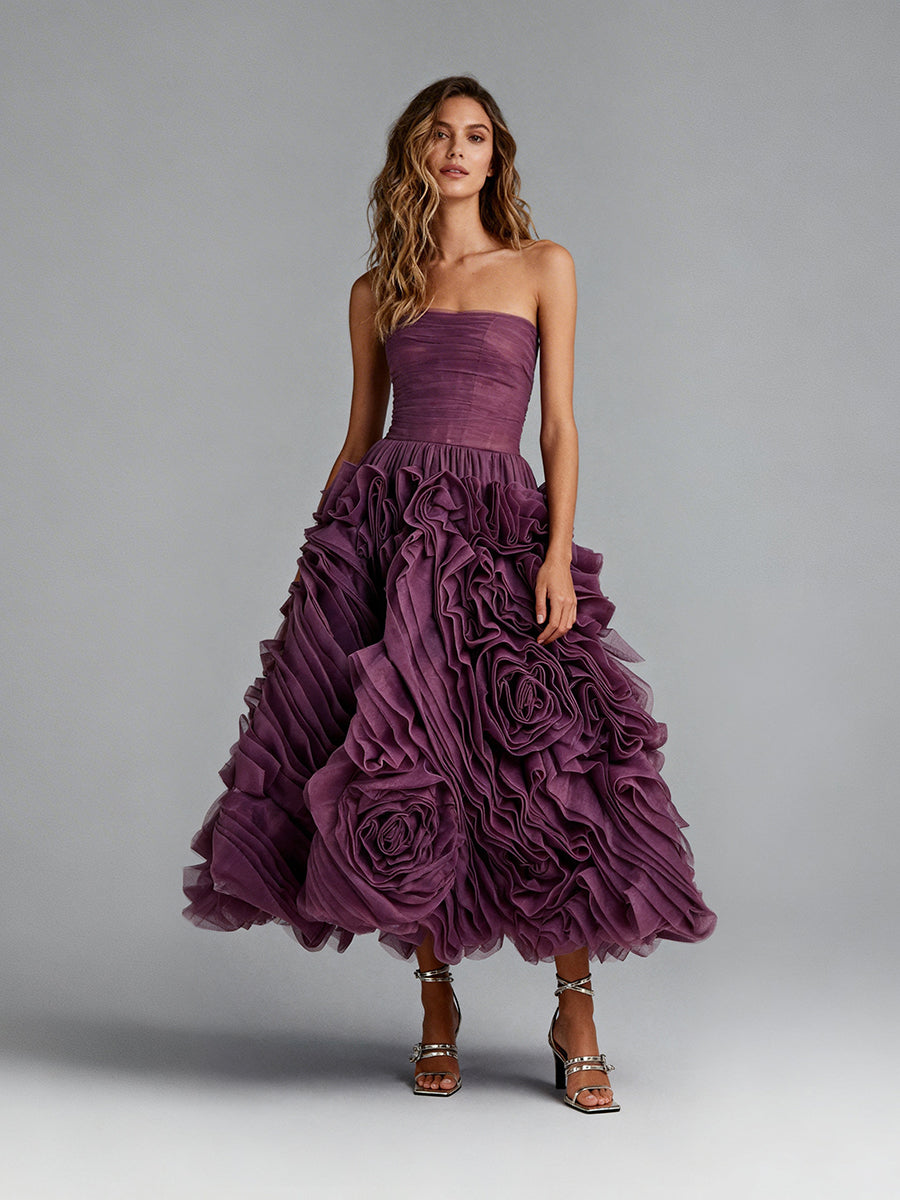 Full front view of a model wearing a plum 3D floral strapless prom dress with a ruffled midi skirt.