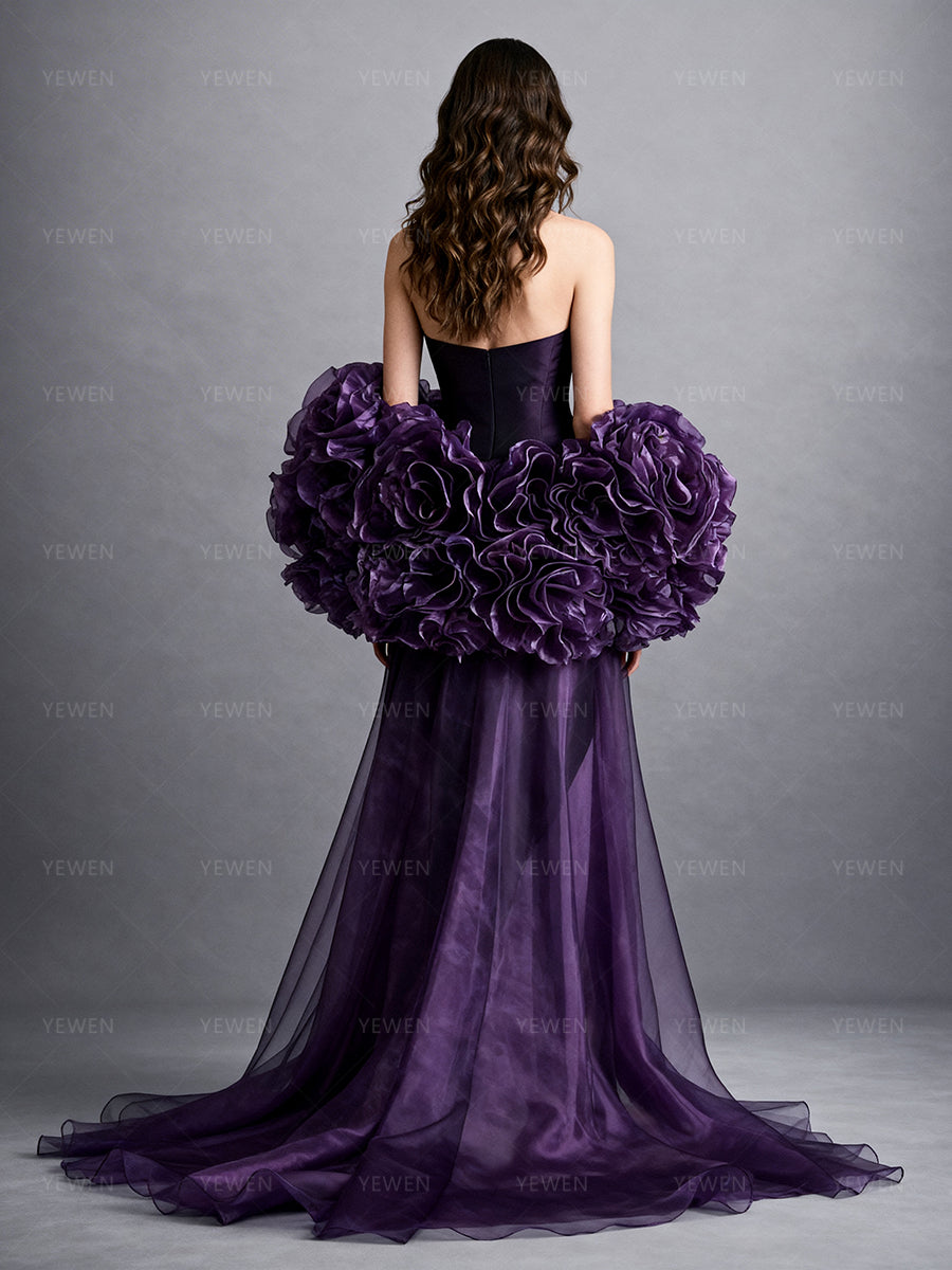 Full back view of a model wearing a purple detachable bridal cape with oversized handmade organza flowers and a flowing sheer train.