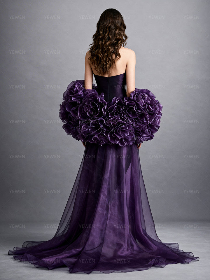 Full back view of a model wearing a purple detachable bridal cape with oversized handmade organza flowers and a flowing sheer train.