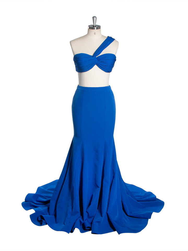 Front view of a royal blue one-shoulder mermaid gown with a twisted bodice and a sweeping train displayed on a mannequin.
