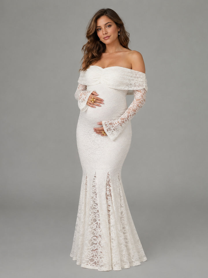 A pregnant model wearing an off-the-shoulder, long-sleeved white lace maternity gown with a fitted bodice and flared lace hem, photographed against a solid gray studio background.