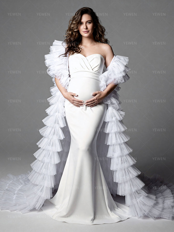 Full front view of a pregnant model wearing a white mermaid maternity photoshoot gown with a strapless sweetheart neckline dramatic sheer ruffle drapes and a layered ruffle train.