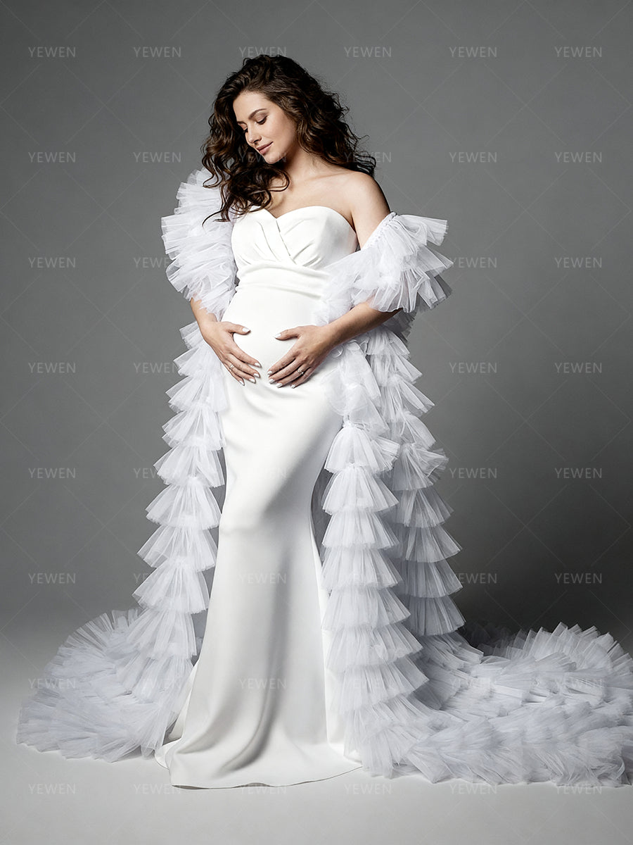 Side view of a pregnant model wearing a white mermaid maternity photoshoot gown with a strapless sweetheart neckline dramatic sheer ruffle drapes and a layered ruffle train.