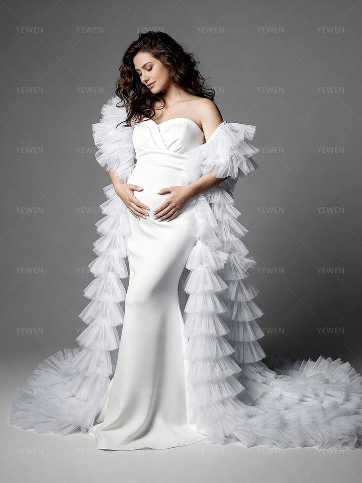 Side view of a pregnant model wearing a white mermaid maternity photoshoot gown with a strapless sweetheart neckline dramatic sheer ruffle drapes and a layered ruffle train.