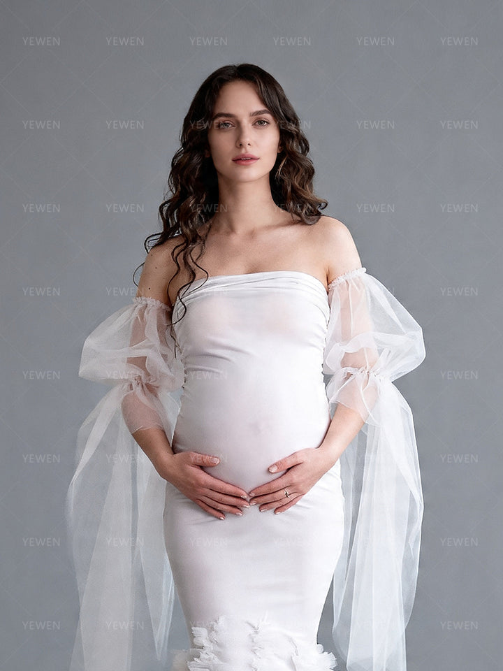 Close-up front view of a pregnant model wearing a white mermaid maternity wedding dress with a strapless sweetheart neckline and sheer arm drapes.