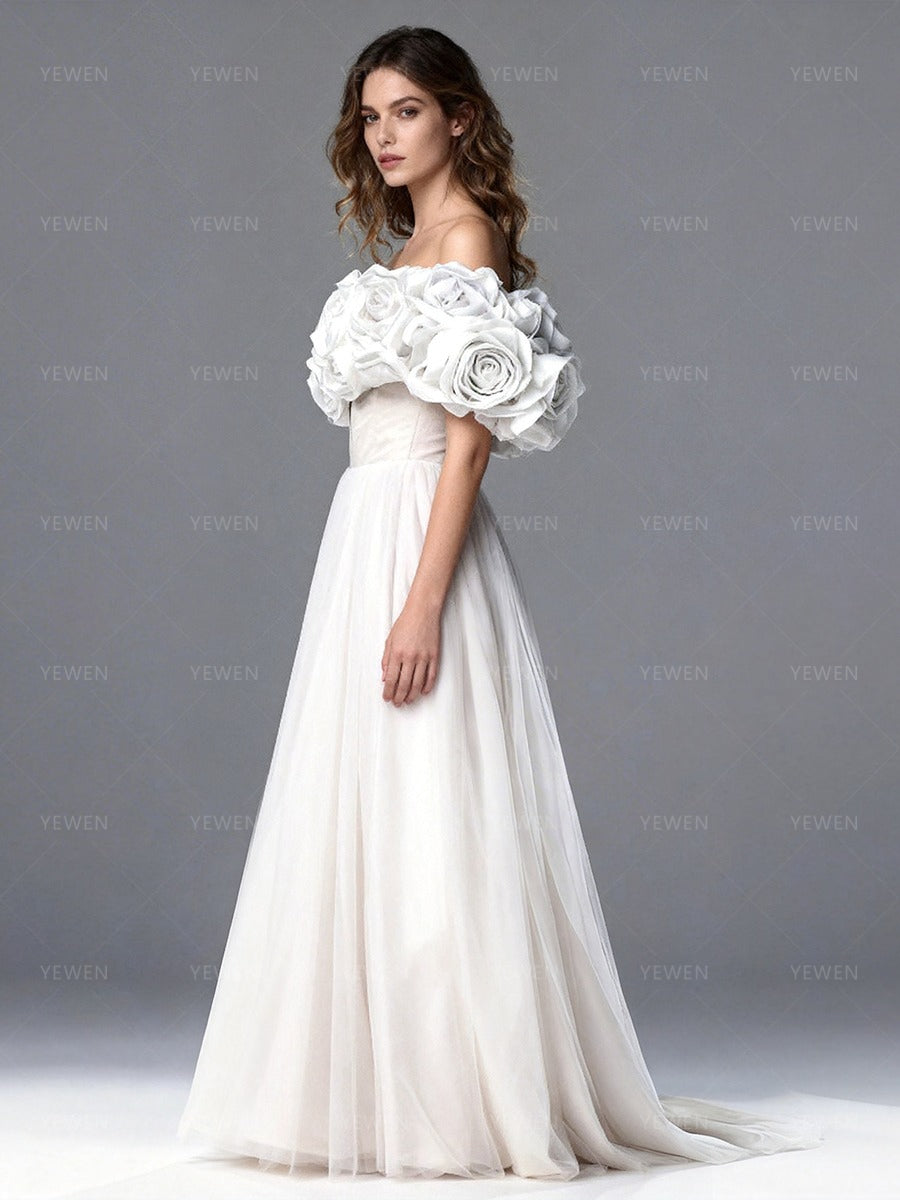 Back view of a model wearing a white off-shoulder tulle gown with a lace-up corset back and sweeping train.