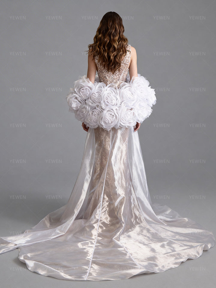 Full back view of a model wearing a white organza wedding cape with oversized floral details and a sweeping sheer train.