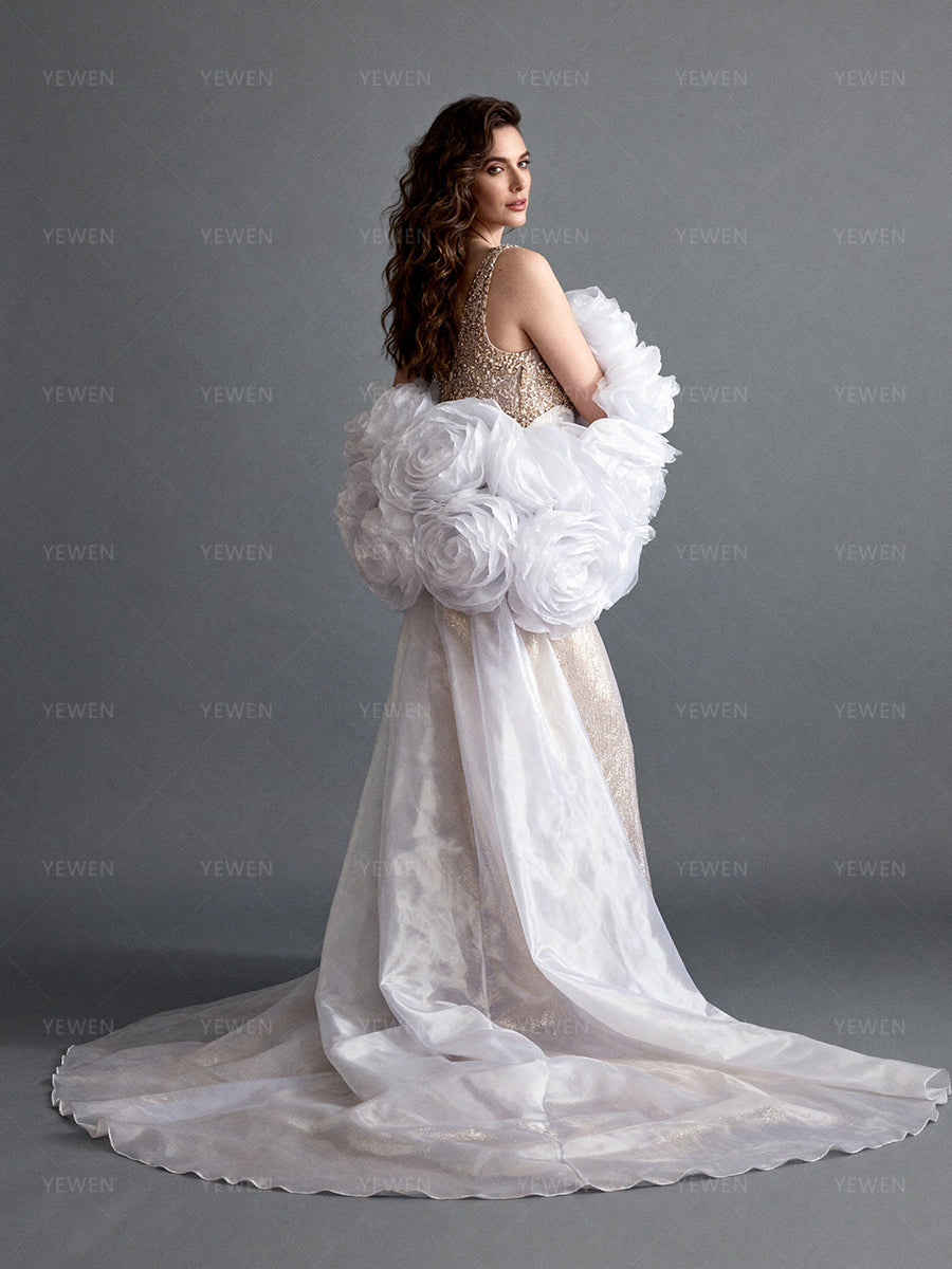 Back side view of a model wearing a white organza wedding cape showing the romantic silhouette and cascading sheer floral train.