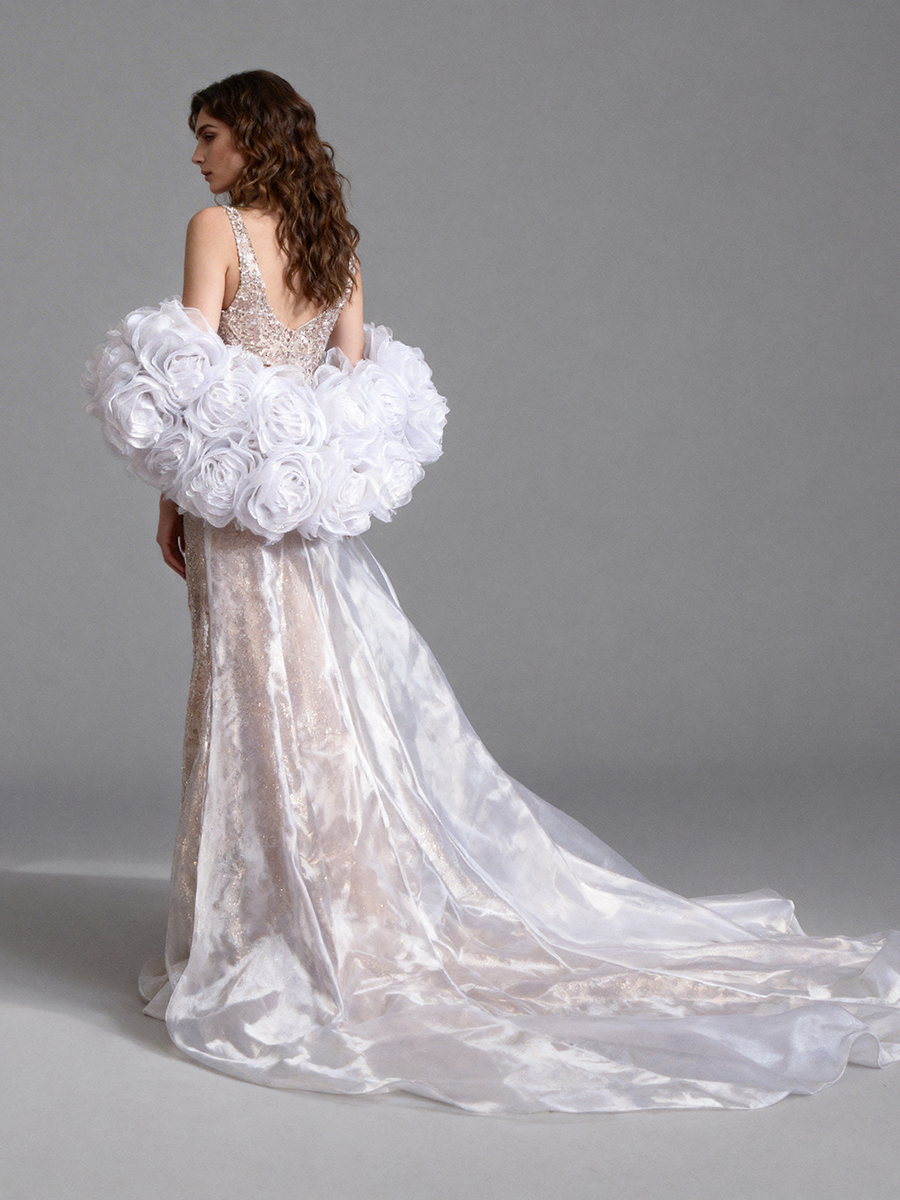 Back view of a model wearing a white organza wedding cape with oversized floral details and a sweeping train.