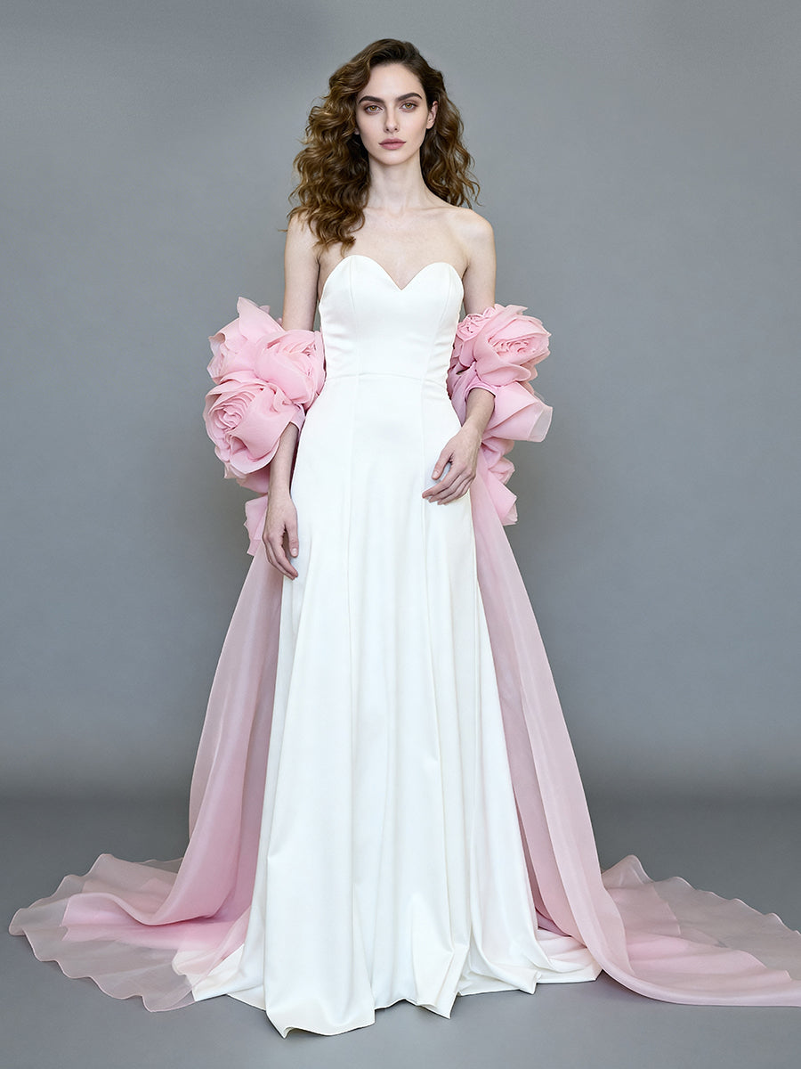 Front view of a model wearing a white formal gown with a pink 3D flower long cape and a sweeping train.