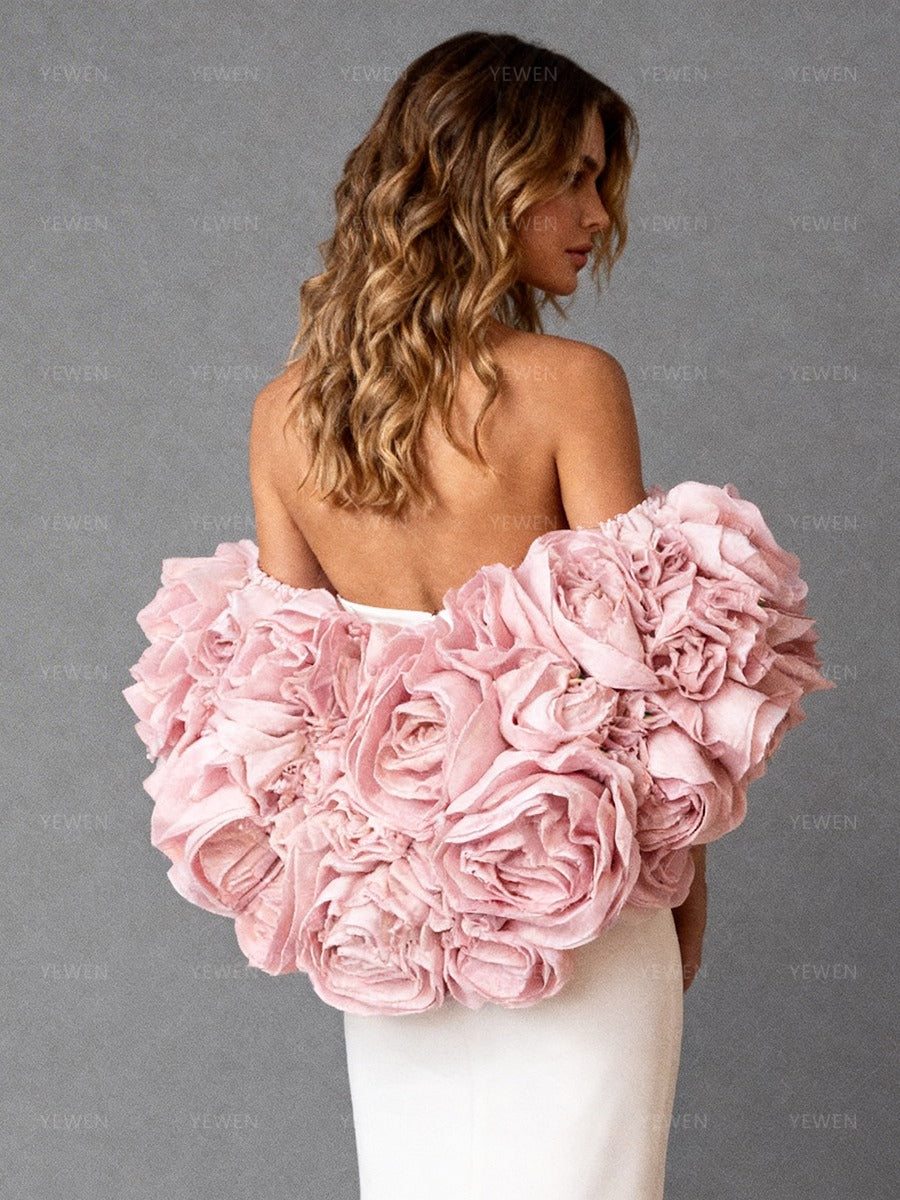 Close-up back view of a model wearing a white strapless formal gown highlighting the pink 3D flower cape and open-back design.