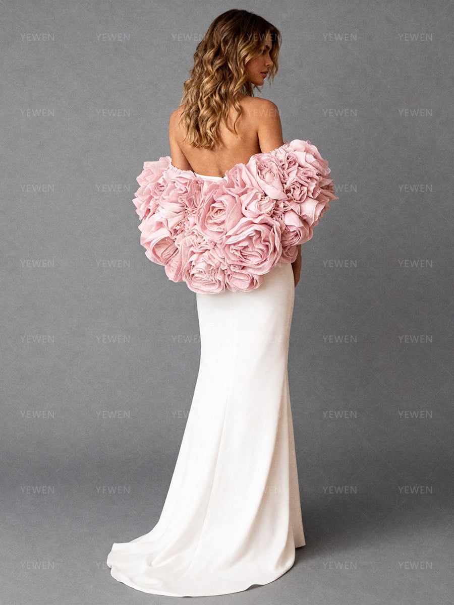 Back view of a model wearing a white strapless formal gown with a pink 3D flower bridal cape and a sweeping train.