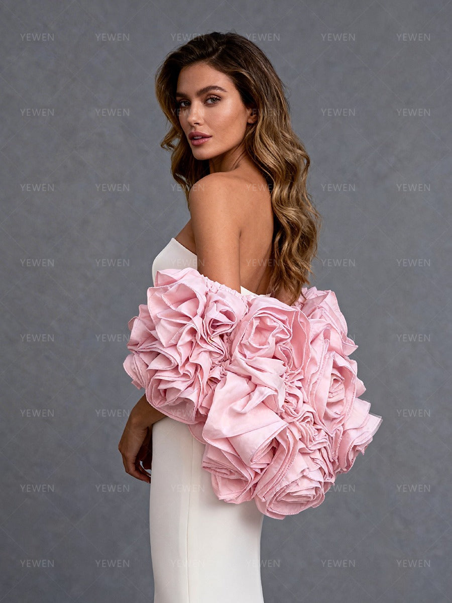 Side close-up view of a model wearing a white strapless formal gown highlighting the pink 3D flower cape and romantic silhouette.