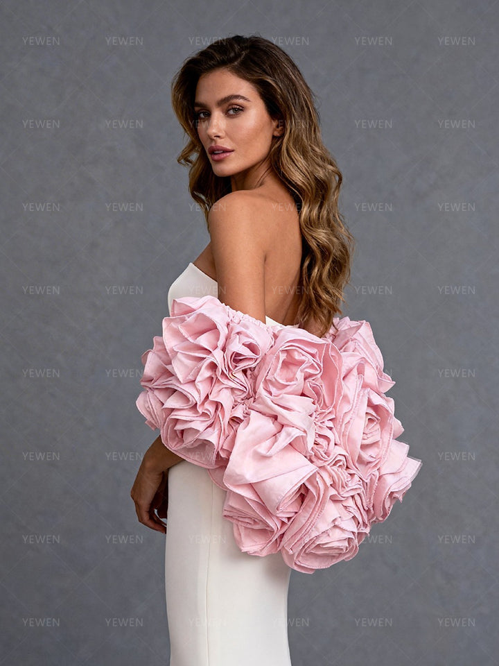 Side close-up view of a model wearing a white strapless formal gown highlighting the pink 3D flower cape and romantic silhouette.