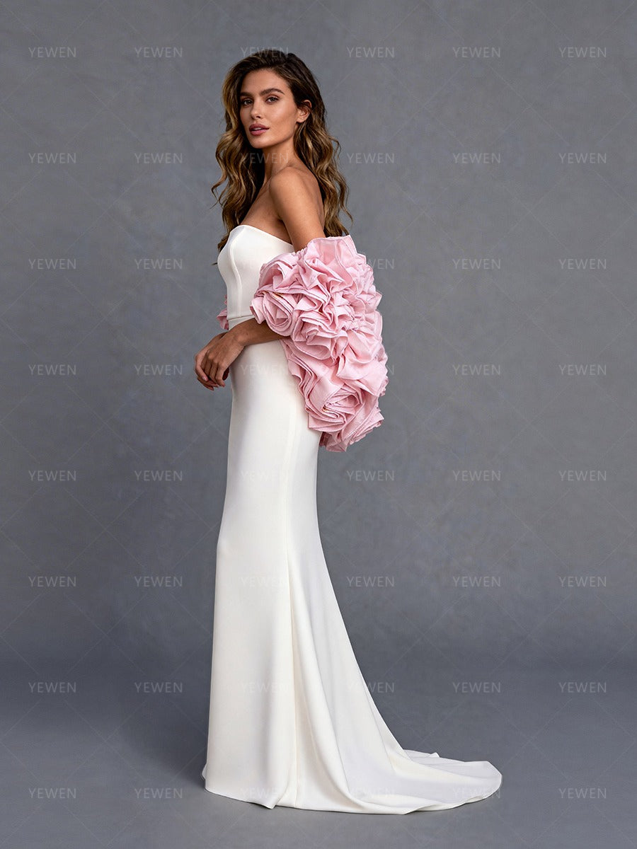 Side view of a model wearing a white strapless formal gown with a pink 3D flower cape showcasing the flowing A-line skirt.