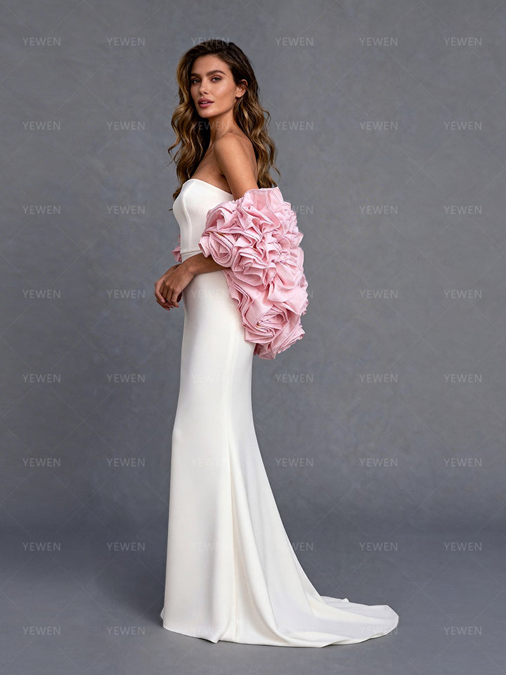 Side view of a model wearing a white strapless formal gown with a pink 3D flower cape showcasing the flowing A-line skirt.