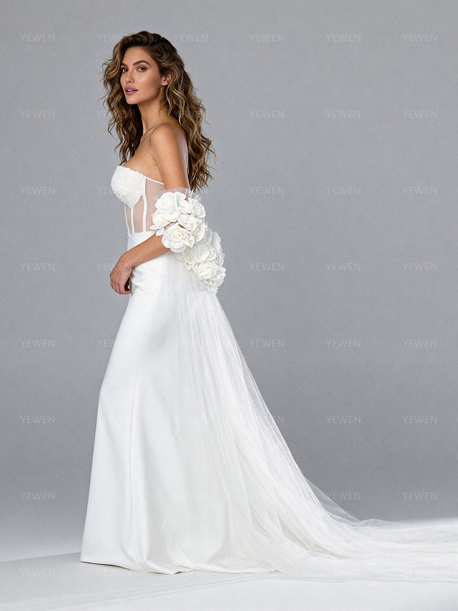 Side view of a model wearing a white tulle bridal cape with handmade floral details and a flowing sheer train.