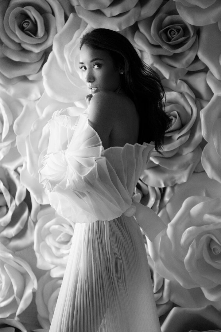 Elegant white pleated maternity photoshoot dress styled in soft light for luxury pregnancy editorial photography